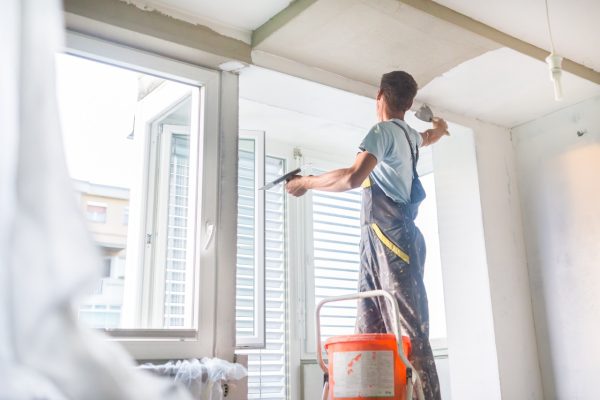 Thirty years old manual worker with wall plastering tools inside a house. Plasterer renovating indoor walls and ceilings with float and plaster.